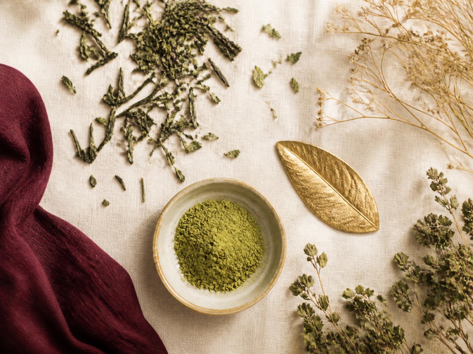 Ingredient flatlay: matcha powder, green tea leaves and gold detail
